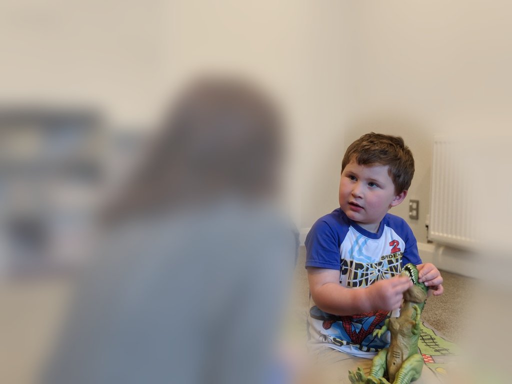 A young boy playing with a toy dinosaur while talking to an adult