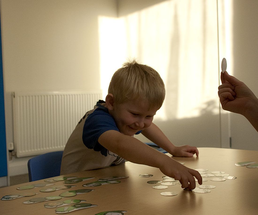 A young boy reaching across a table of picture cards during a speech therapy session